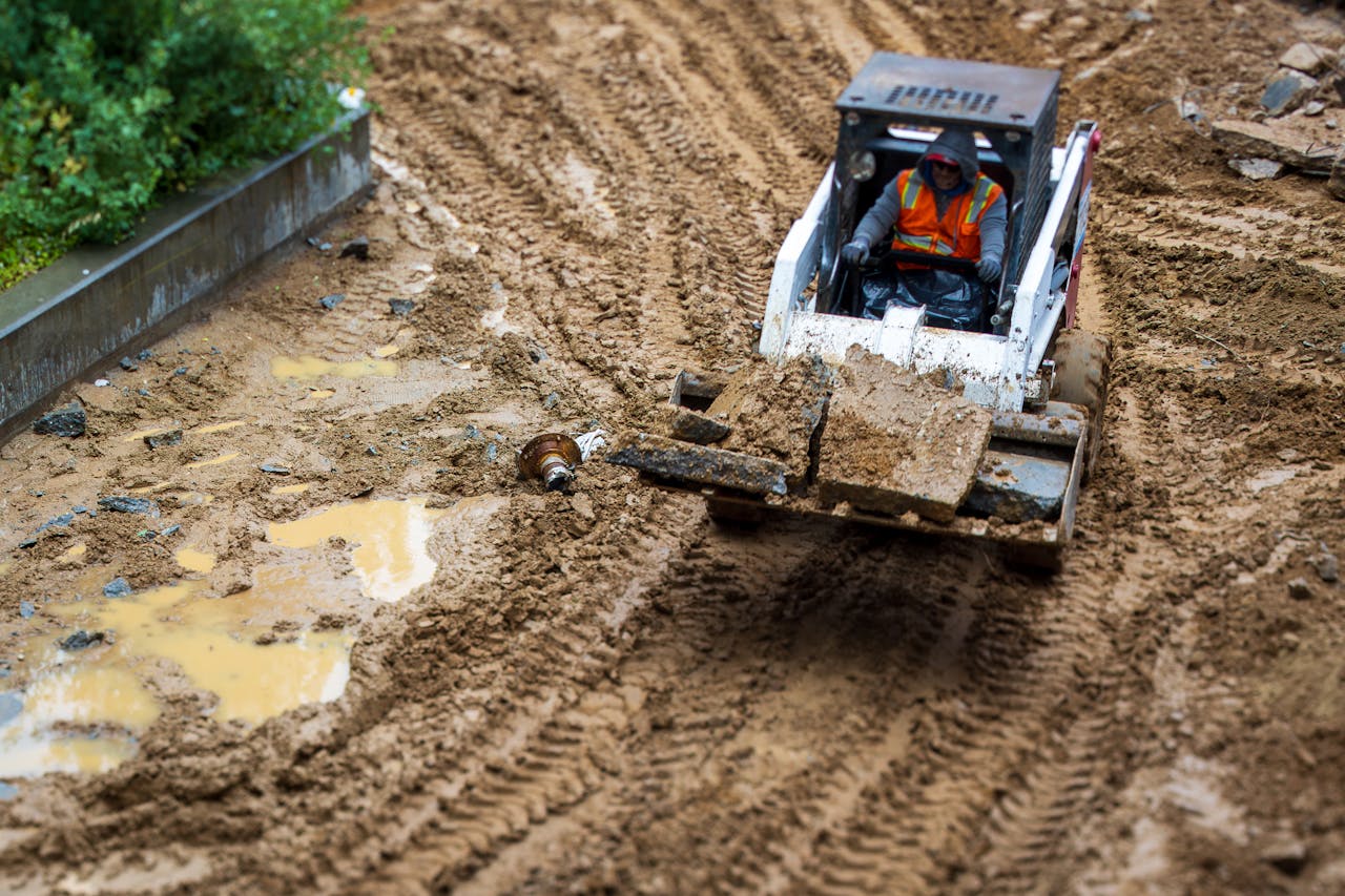 A worker operates a backhoe in a muddy construction site, showcasing heavy machinery in action.